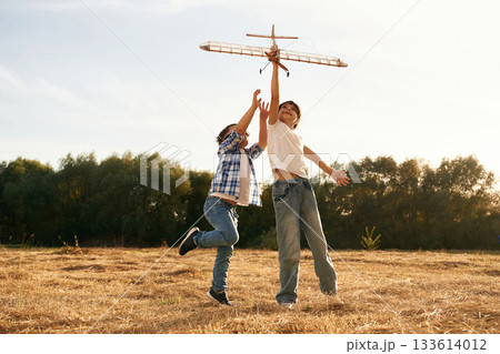 Flying high up. Boy and girl are playing with wooden toy plane on the field Flying high up. Boy and girl are playing with wooden toy plane on the field 133614012