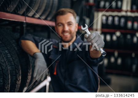 Wrench is in the hand. Man worker is maintenance station with tires, wheels Wrench is in the hand. Man worker is maintenance station with tires, wheels 133614245