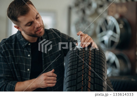 With measuring tool. Man worker is maintenance station with tires, wheels With measuring tool. Man worker is maintenance station with tires, wheels 133614333