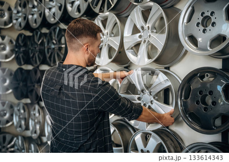 Choosing the right disk. Man worker is maintenance station with tires, wheels Choosing the right disk. Man worker is maintenance station with tires, wheels 133614343