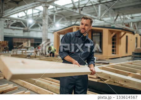 Wooden plank in hands. Male builder is at construction of house 133614567