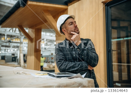 In white helmet. Male builder is at construction of wooden house 133614643