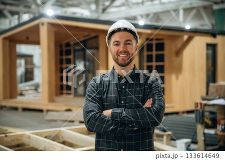 Cheerful facial expression. Male builder is at construction of wooden house Cheerful facial expression. Male builder is at construction of wooden house 133614649