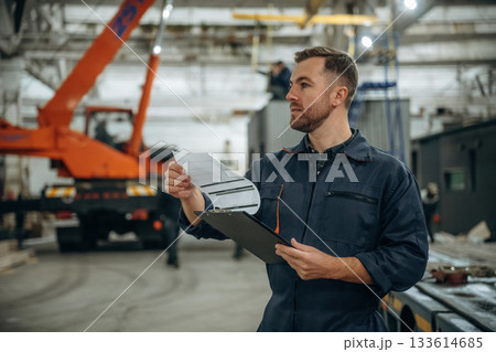 Front view, holding notepad, standing. Male worker is in the modern warehouse or manufacturing company Front view, holding notepad, standing. Male worker is in the modern warehouse or manufacturing company 133614685
