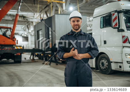 Front view, standing. Male worker is in the modern warehouse or manufacturing company Front view, standing. Male worker is in the modern warehouse or manufacturing company 133614689