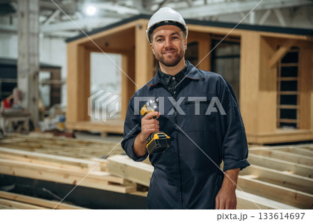 Small drill in hands. Male builder is at construction of wooden house Small drill in hands. Male builder is at construction of wooden house 133614697