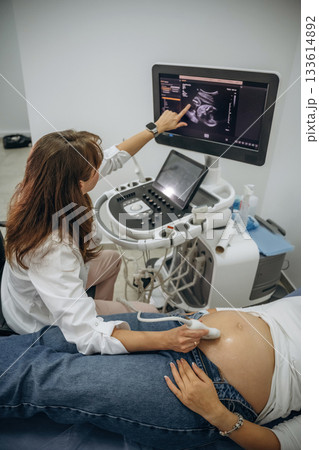 Monitor with graphical representation of scan. Pregnant woman undergoing ultrasound test Monitor with graphical representation of scan. Pregnant woman undergoing ultrasound test 133614892