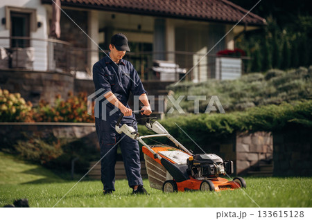 Fuel powered lawn mover, cutting the grass. Professional gardener is on the lawn 133615128