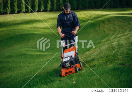 Process of cutting the grass by using lawn mover. Professional gardener is on the lawn Process of cutting the grass by using lawn mover. Professional gardener is on the lawn 133615145