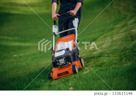 Process of cutting the grass by using lawn mover. Professional gardener is on the lawn Process of cutting the grass by using lawn mover. Professional gardener is on the lawn 133615146