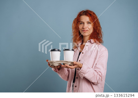 White cups of drinks, holding it. Woman is in the studio against background 133615294