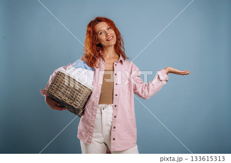Thinking, holding washed clothes in a basket. Woman is in the studio against background 133615313