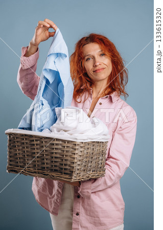 Basket with cleaned fresh clothes. Woman is in the studio against background 133615320