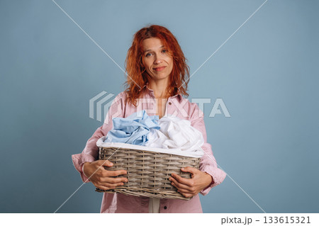 Basket with cleaned fresh clothes. Woman is in the studio against background 133615321