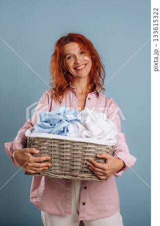 Cheerful facial expression, holding washed fresh clothes. Woman is in the studio against background Cheerful facial expression, holding washed fresh clothes. Woman is in the studio against background 133615322
