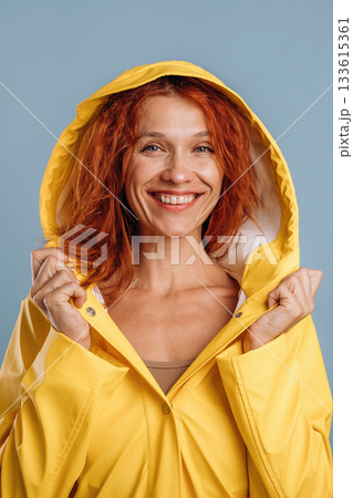 Smiling, in yellow raincoat. Woman is in the studio against background 133615361
