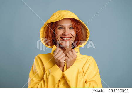 Smiling, in yellow raincoat. Woman is in the studio against background 133615363