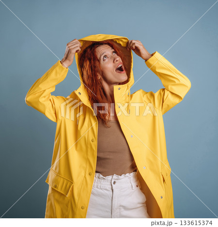 Looking for a rain, in yellow coat. Woman is in the studio against background Looking for a rain, in yellow coat. Woman is in the studio against background 133615374