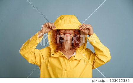 Having fun, in yellow raincoat, smiling. Woman is in the studio against background 133615382