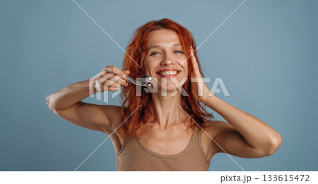 Using massager to take care of face skin. Woman is in the studio against background Using massager to take care of face skin. Woman is in the studio against background 133615472