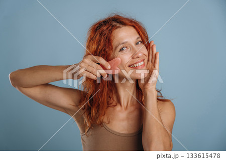 Pink colored face patch being used on the skin. Woman is in the studio against background 133615478