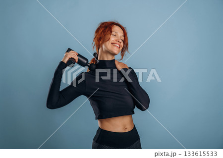 Black electric massager, in fitness clothes. Woman is in the studio against background 133615533