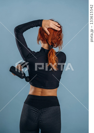 Process of using electric massager, in sportive fitness clothes. Woman is in the studio against background Process of using electric massager, in sportive fitness clothes. Woman is in the studio against background 133615542