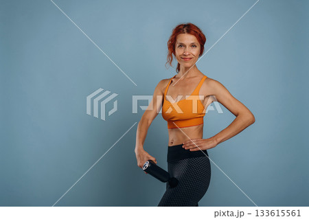Automatic massager is being used. In sport clothes. Woman is in the studio against background 133615561