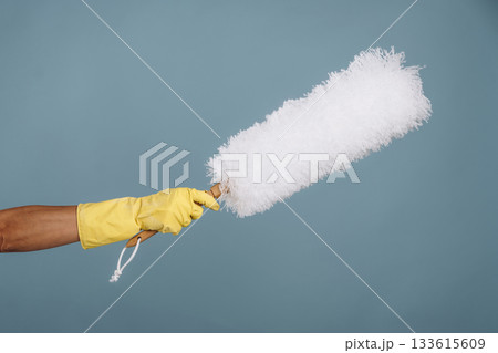 Maid is holding dust brush against blue background Maid is holding dust brush against blue background 133615609