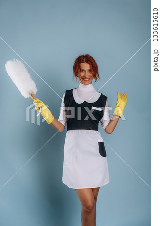 Maid is with dust brush. Woman is in the studio against background Maid is with dust brush. Woman is in the studio against background 133615610
