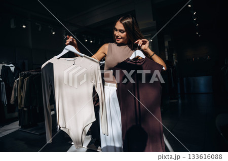 Illuminated by sunlight, darkened. Woman chooses clothes in retail store Illuminated by sunlight, darkened. Woman chooses clothes in retail store 133616088