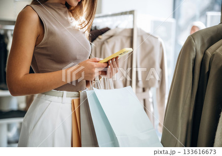 Smartphone in hands. Close up view of woman that is chooses clothes in the retail shop 133616673