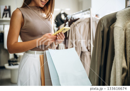 Smartphone in hands. Close up view of woman that is chooses clothes in the retail shop Smartphone in hands. Close up view of woman that is chooses clothes in the retail shop 133616674