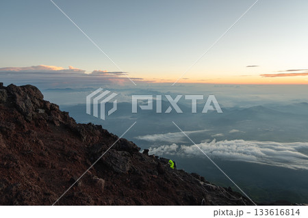On Mount Fuji, Kitayama, Fujinomiya, Shizuoka, Japan, Hiker climbing rocky mountain slope at sunrise with scenic valley view On Mount Fuji, Kitayama, Fujinomiya, Shizuoka, Japan, Hiker climbing rocky mountain slope at sunrise with scenic valley view 133616814
