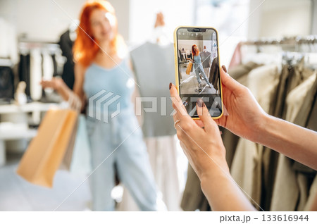 Making a photo by using smartphone. Two female friends are in the retail store, choosing clothes, shopping 133616944
