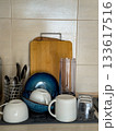Freshly washed dishes drying on a kitchen counter with cups, bowls, utensils, and cutting boards. 133617516