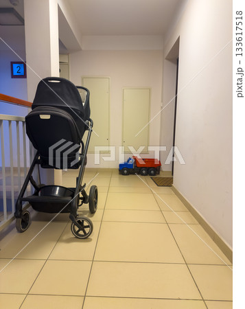 Baby stroller and toy truck left in an apartment hallway with tile floor and stairway rail. Baby stroller and toy truck left in an apartment hallway with tile floor and stairway rail. 133617518