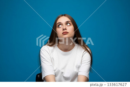 Young woman showing a skeptical doubtful expression while shrugging in a blue studio portrait Young woman showing a skeptical doubtful expression while shrugging in a blue studio portrait 133617627