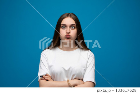 Expressive young woman posing with a confused facial expression against a bright blue studio background Expressive young woman posing with a confused facial expression against a bright blue studio background 133617629
