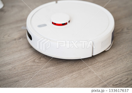 Top view of robotic vacuum cleaner moving across wooden floor while performing automated home cleaning Top view of robotic vacuum cleaner moving across wooden floor while performing automated home cleaning 133617637