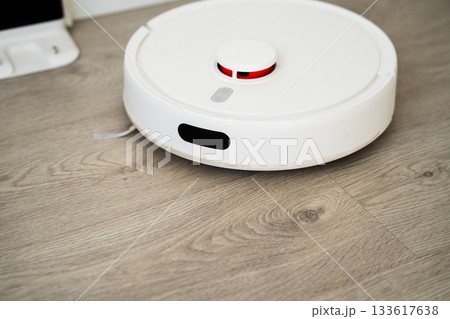 Front view of smart robotic vacuum cleaner on wooden floor performing automated home cleaning task Front view of smart robotic vacuum cleaner on wooden floor performing automated home cleaning task 133617638
