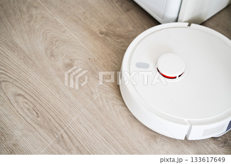 Top view of robot vacuum cleaner on wooden floor showing round design and bright interior setting 133617649