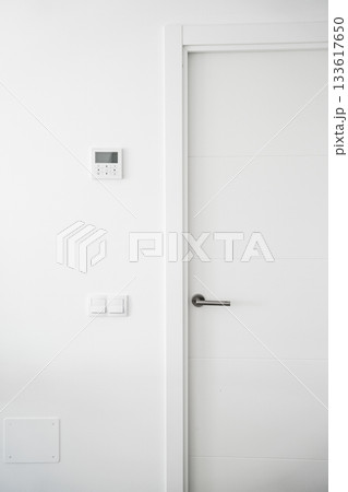Minimalist white interior wall with modern thermostat, light switches and clean door design Minimalist white interior wall with modern thermostat, light switches and clean door design 133617650