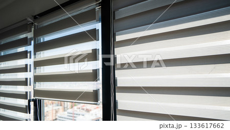 Striped zebra roller blinds on large windows providing adjustable light control in modern bright interior 133617662
