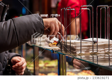 Customer reaching for a white napkin from a metal holder while vendors work behind the counter at a winter street food market Customer reaching for a white napkin from a metal holder while vendors work behind the counter at a winter street food market 133619271
