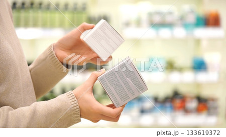 Female shopper reading ingredient labels, comparing and choosing a cosmetic product or cream, focusing on packaging details in a beauty store. The concept of conscious choice 133619372