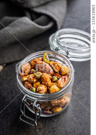 Nuts coated in sugar glaze in jar on black table. 133619965