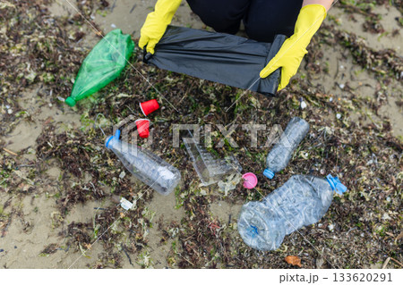 volunteer collecting plastic bottles on a polluted beach, highlighting ocean pollution, waste problem, environmental protection and coastal cleanup action. volunteer collecting plastic bottles on a polluted beach, highlighting ocean pollution, waste problem, environmental protection and coastal cleanup action. 133620291