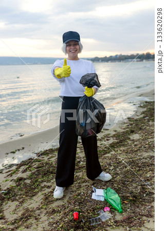 Volunteer collecting beach litter into a black trash bag during coastal cleanup, highlighting pollution, waste problem, environmental protection and eco awareness. 133620298