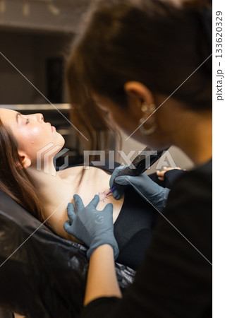 tattoo artist working on a woman chest design in a studio, showing the process of professional tattooing, precision, sterile gloves and cosmetic procedure atmosphere. 133620329